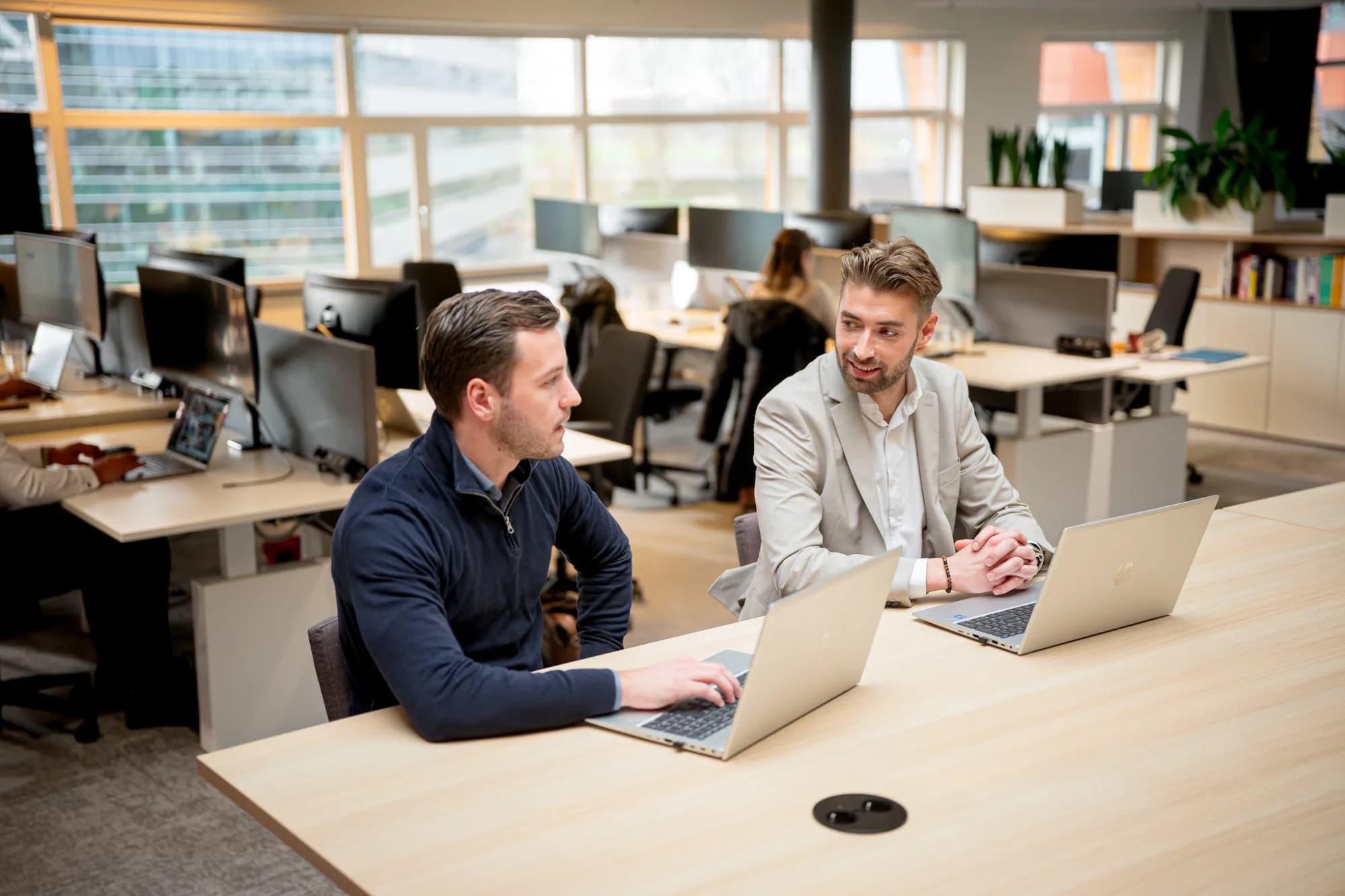 Twee personen in meeting op kantoor met laptops, overleg over strategisch partnerschap.
